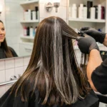Femme aux cheveux bruns avec racines grises en cours de balayage chez un coiffeur professionnel
