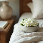 Bol en céramique rempli de fleurs de jasmin de Bali posé sur une table de nuit en bois, ambiance chambre à coucher apaisante pour le sommeil naturel