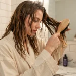 Jeune femme aux cheveux ondulés utilisant une brosse à palette en bois dans sa salle de bain lors de sa routine du soir