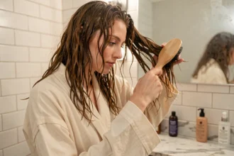 Jeune femme aux cheveux ondulés utilisant une brosse à palette en bois dans sa salle de bain lors de sa routine du soir