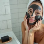Femme appliquant du savon noir sur son visage à peau grasse dans une salle de bain minimaliste